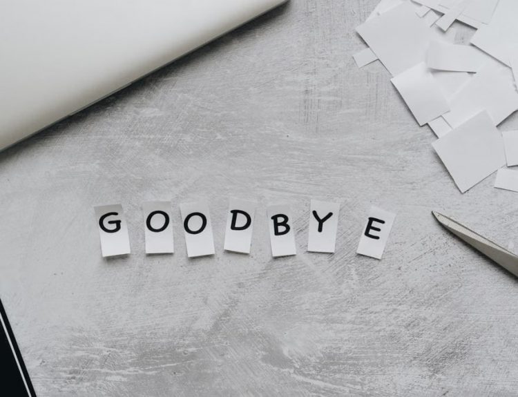 Artistic flat lay featuring the word 'GOODBYE' crafted from paper cutouts with scissors and a laptop.