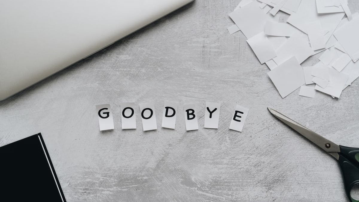 Artistic flat lay featuring the word 'GOODBYE' crafted from paper cutouts with scissors and a laptop.