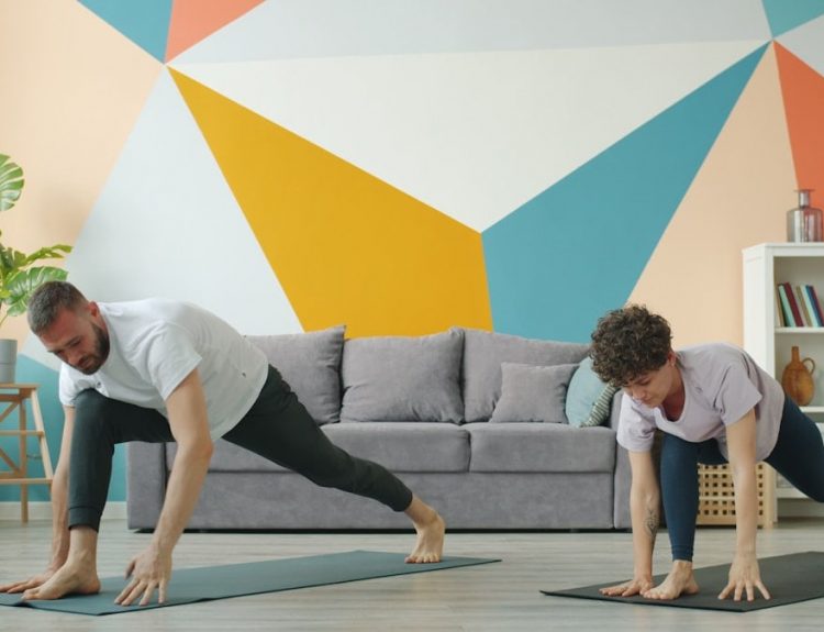 Woman and man are working out at home doing yoga together synchronously on mats caring for body health. Modern people, sports and apartment concept.