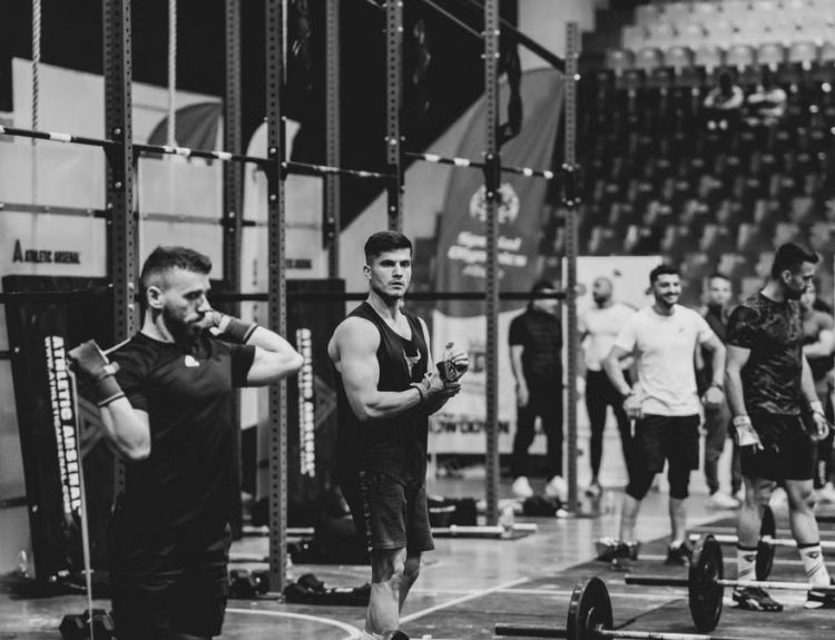 Black and white image of a fitness competition showcasing athletes and weights in a gym setting.